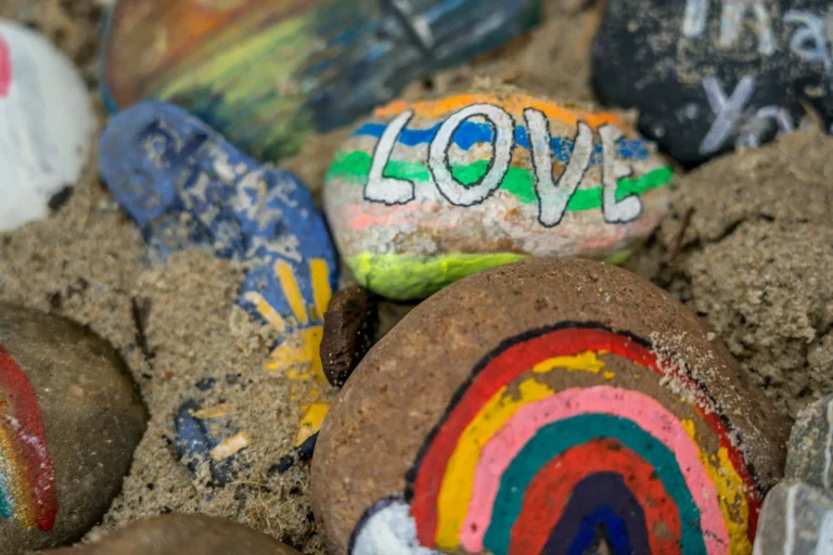 three stones, one with a rainbow painted on, one with the words love painted on and one painted blue with the sun