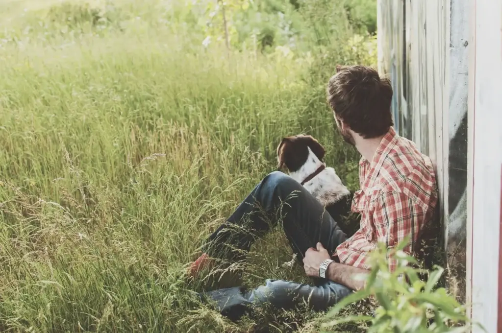 man sittin in a field next to his dog
